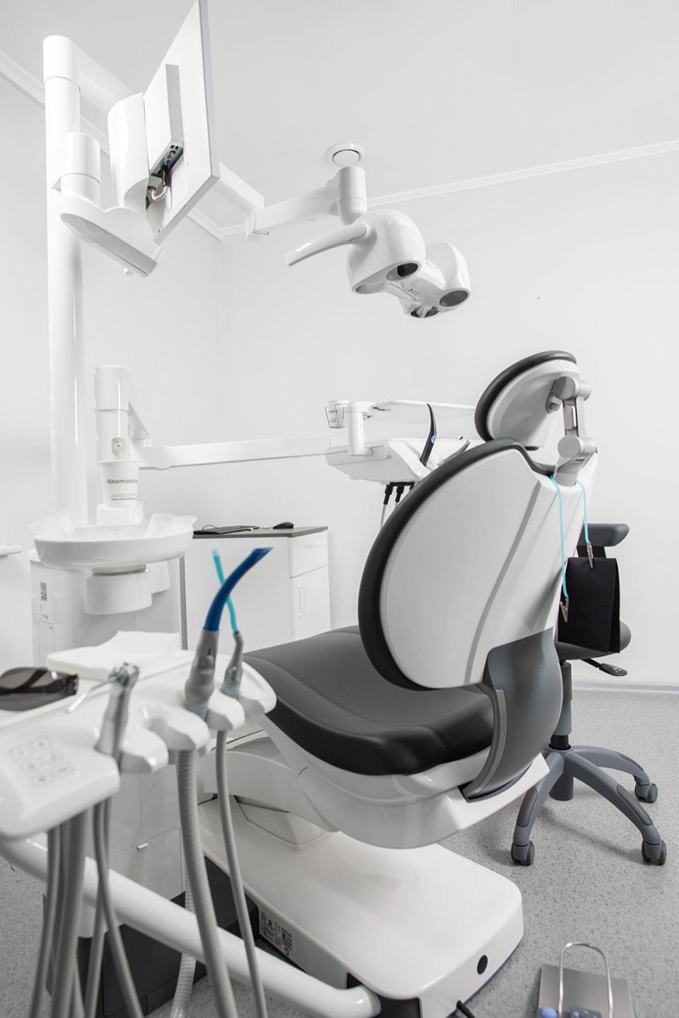 A bright dental treatment room with a grey chair, overhead light and equipment; stock design reference only.